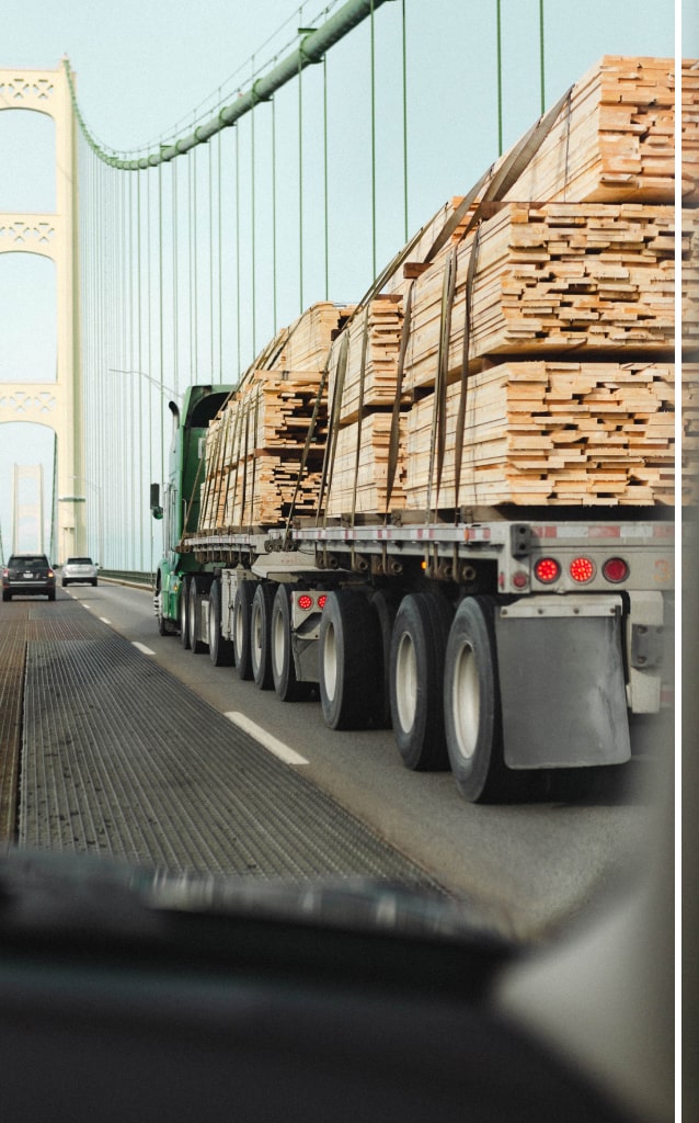 Green flatbed truck transporting pine boards on a bridge.