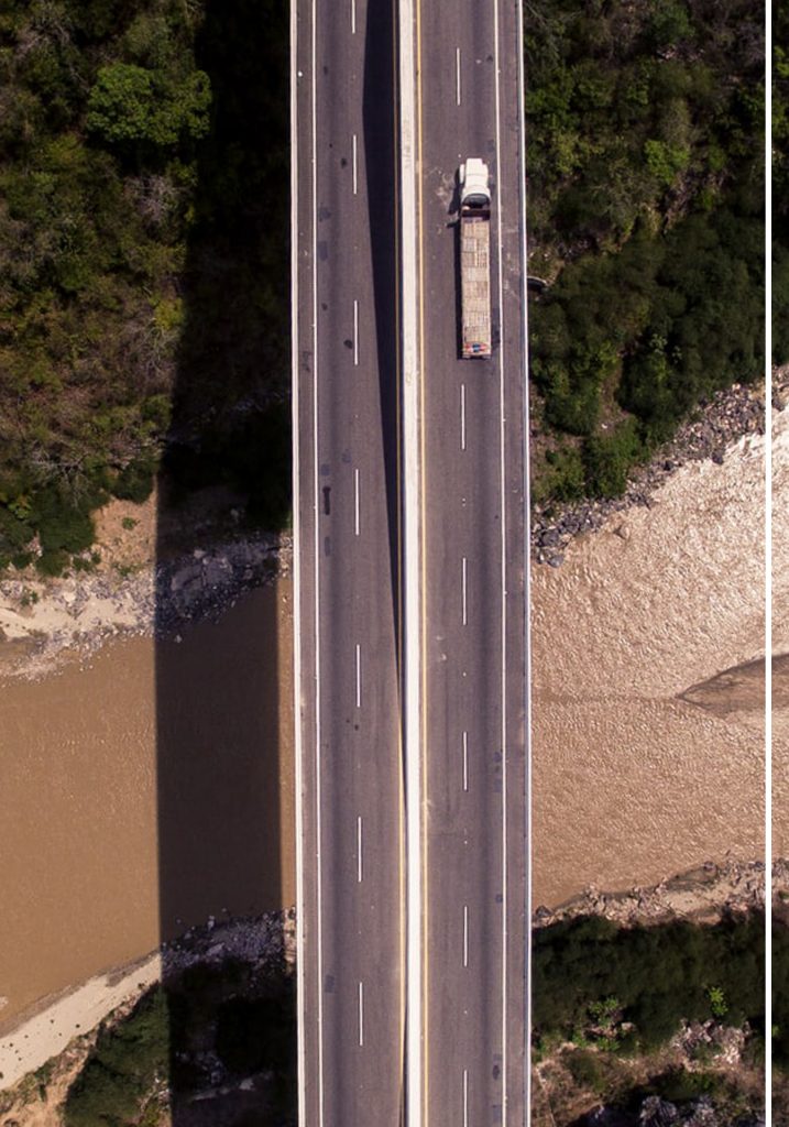 A view from the sky of a bridge over water with a trailer driving through it.